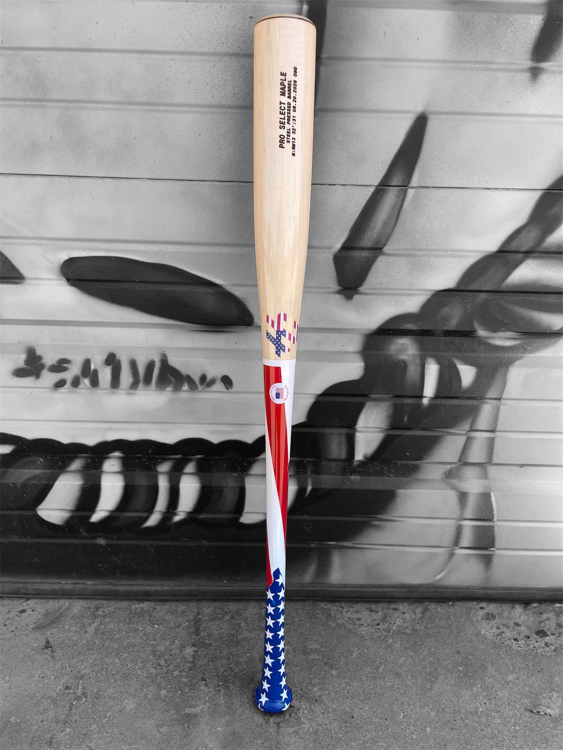 American flag HC Bats RM13 Pro Select Maple baseball bat with stars and stripes handle and natural barrel displayed horizontally on a white background.
