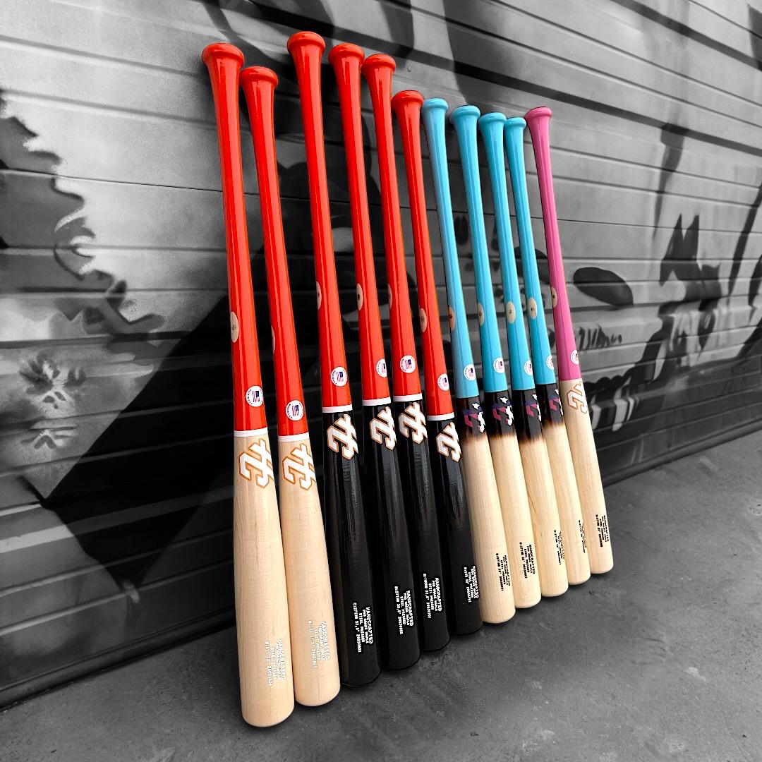 Row of baseball bats with red, black, blue, and pink handles against a gray background, custom made in odessa texas