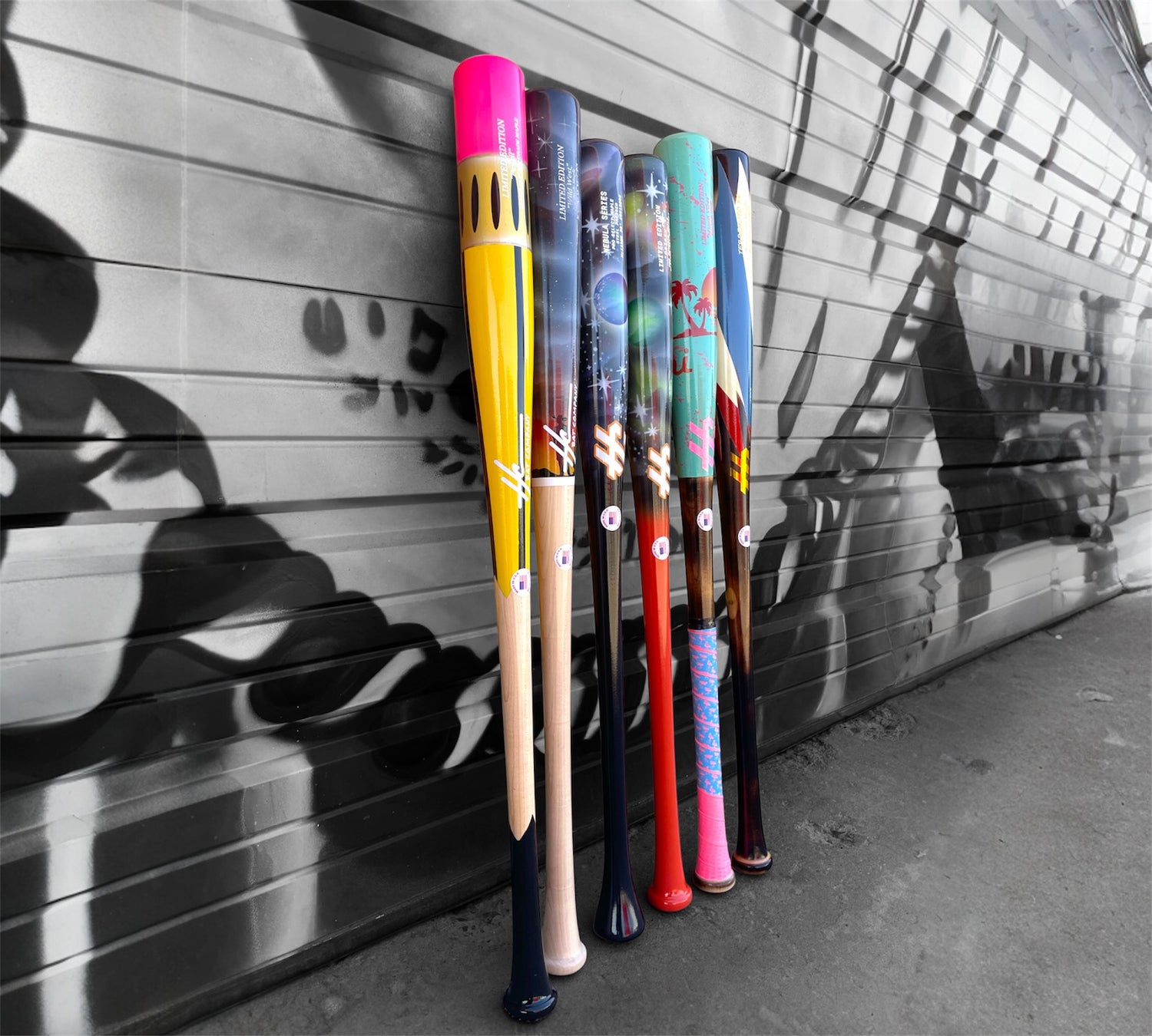 Colorful baseball bats leaning against a textured wall with graffiti.