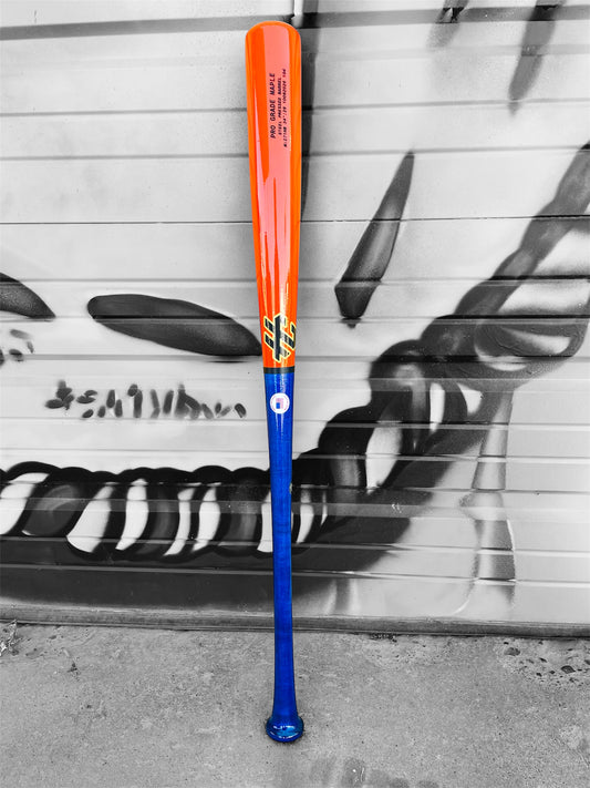 HC Bats 271HB 34-inch Pro Grade Maple baseball bat with royal blue handle and neon orange barrel standing upright against a black and white graffiti-covered garage door.
