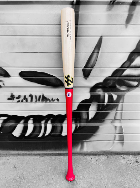 HC Bats Model 180 33-inch 30 oz Pro Grade Maple baseball bat with bright hot pink handle and natural maple barrel standing upright against a black and white graffiti-covered garage door.