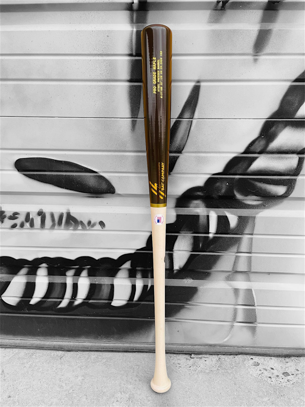 HC Bats 271HB 32-inch 28 oz Pro Grade Maple baseball bat with natural handle and glossy espresso brown barrel standing upright in front of a black and white graffiti wall.
